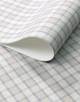 Close-up of vintage plaid check wallpaper in soft beige and grey-blue tones with a linen surface, partially rolled to show paper thickness.