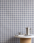 Interior scene with vintage plaid check linen wallpaper in blue and beige tones, styled with a marble and cork table and brushed metal coffee accessories.