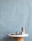 Interior scene showcasing vintage blue plaid check linen wallpaper, paired with a marble and cork pedestal table and stainless steel coffee accessories.