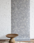 Wallpaper with floral pattern on a white brick wall with a wooden table in front.