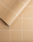 Beige wallpaper with a white grid pattern, partially unrolled to display its smooth, matte texture and precise geometric square design.