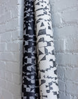 Rolled black and white wallpaper with matching abstract black geometric patterns, leaning against a white brick wall.