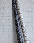 Rolled black and white wallpaper featuring abstract black geometric shapes, propped against a white brick wall.