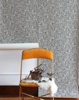 Interior space with a black and white botanical wallpaper roll partially hung on the wall, styled with a mustard velvet chair and a small potted plant.