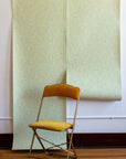 Minimalist interior featuring soft green botanical wallpaper with a fine leaf pattern, paired with a mustard velvet chair for a subtle and elegant contrast.