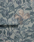Rolled section of silk wallpaper showcasing a botanical pattern with blue leaves and beige flowers, emphasizing its texture and organic flow.