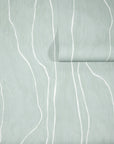 Soft sage green wallpaper with abstract white vertical wavy lines, partially unrolled to reveal texture and pattern.