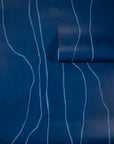 Deep navy blue wallpaper with abstract light blue wavy vertical lines, partially unrolled to showcase the pattern.