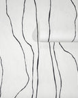 Crisp white wallpaper with bold black wavy vertical lines, partially unrolled to display the abstract pattern.