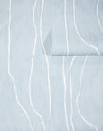 Light blue wallpaper with abstract white wavy vertical lines, partially unrolled to showcase the soft, organic pattern.