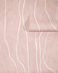Soft blush-toned wallpaper with flowing white wavy vertical lines, partially unrolled to reveal its organic and elegant pattern.