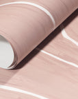 Rolled-up blush wallpaper with soft white wavy stripes, highlighting its smooth texture and sophisticated design.