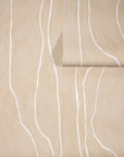Warm beige wallpaper with abstract white wavy vertical lines, partially unrolled to showcase its natural and earthy aesthetic.