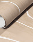 Rolled-up beige wallpaper with organic white wavy stripes, emphasizing its soft texture and timeless design.