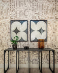 Contemporary living space with abstract beige and taupe brushstroke grasscloth wallpaper, a sleek black console table, and two symmetrical geometric framed artworks.