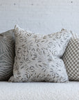 Cream and gray botanical leaf pillow styled with silver gray sunburst and cream checkerboard pillows on white boucle sofa