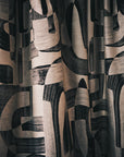 Black and tan abstract jacquard fabric hung as floor-length curtains shown close up in deep folds