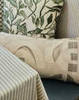 Tan abstract print linen fabric made up as a bolster pillow layered with pillows in a breakfast nook