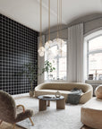 Modern living room with a white and black square grid patterned wallpaper, curved beige sofa, plush accent chair, and sculptural pendant lighting, creating a contemporary and elegant ambiance.