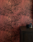 Dramatic botanical wallpaper in a deep rust-red hue with intricate foliage illustrations, styled with a dark wooden cabinet and minimalist decor.