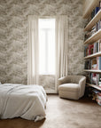 Serene bedroom featuring a soft taupe botanical wallpaper, paired with neutral bedding, a plush beige armchair, and wooden bookshelves for a tranquil, cozy retreat.