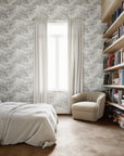 Cozy bedroom featuring a textured botanical wallpaper in white complemented by a neutral bedspread, cream-colored armchair, and built-in wooden bookshelves.