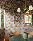 Dining room with multi-colored floral wallpaper covering walls and ceiling, featuring pink, green, and purple leaf patterns; green marble table, wicker chairs, and rustic chandelier with white shades in the foreground.