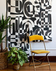2 Drops of Down the Rabbit Hole Wallpaper on an office wall with yellow velvet folding chair and two house plants