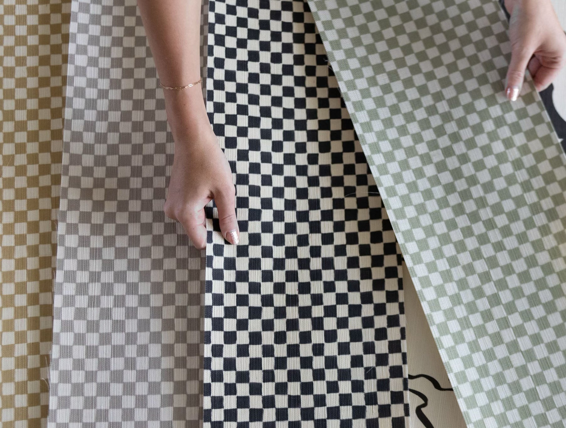 Printed checker board grasscloth wallpaper with woman&#39;s hand holding swatches of material