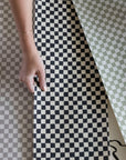 A selection of checkered wallpaper swatches in neutral tones, including beige, taupe, black, and green, displayed with a hand showcasing their texture.
