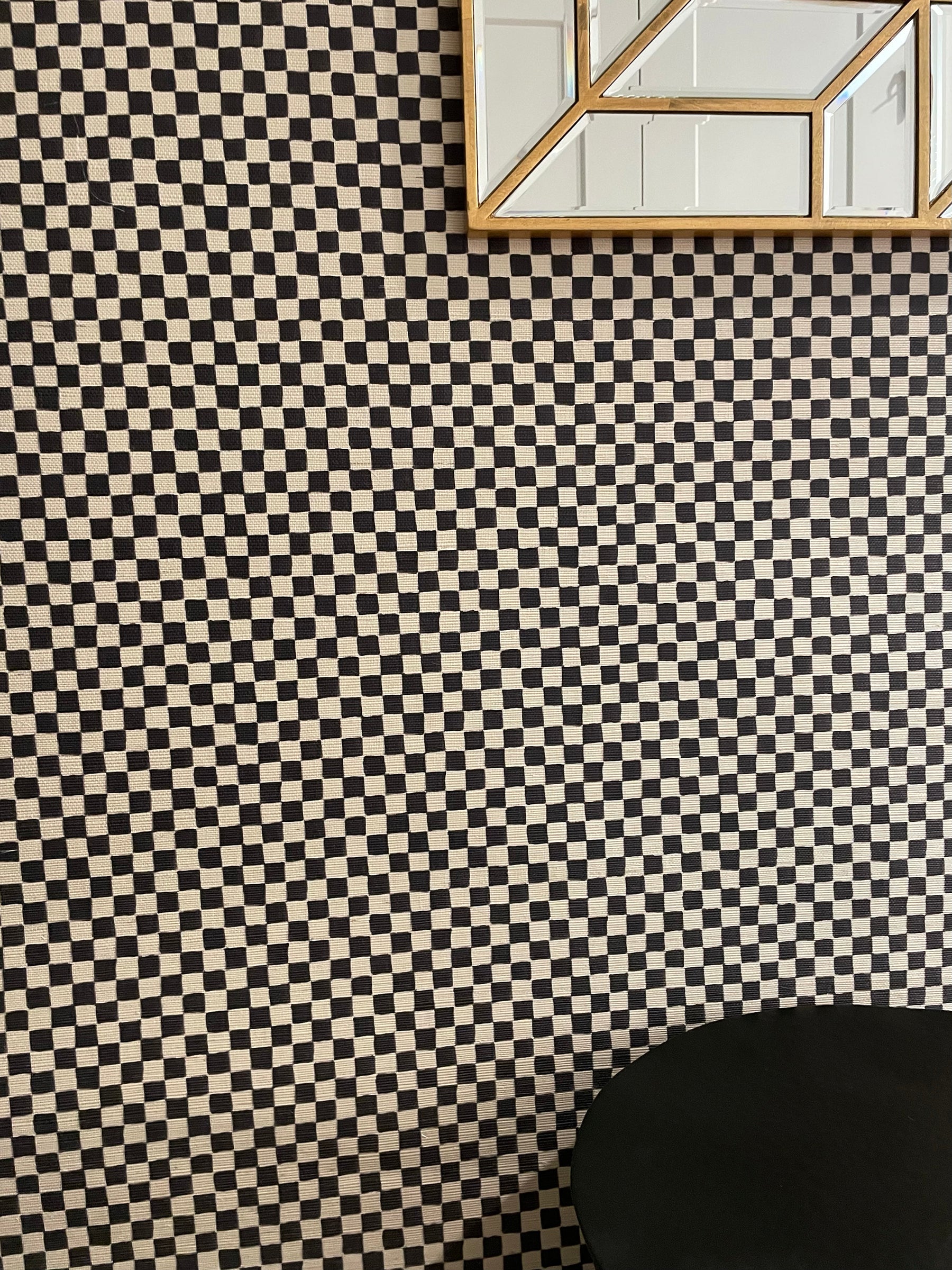 Modern interior with black and beige wavy checkered wallpaper, a geometric mirror with a gold frame, and a sleek black table.