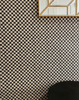 Modern interior with black and beige wavy checkered wallpaper, a geometric mirror with a gold frame, and a sleek black table.