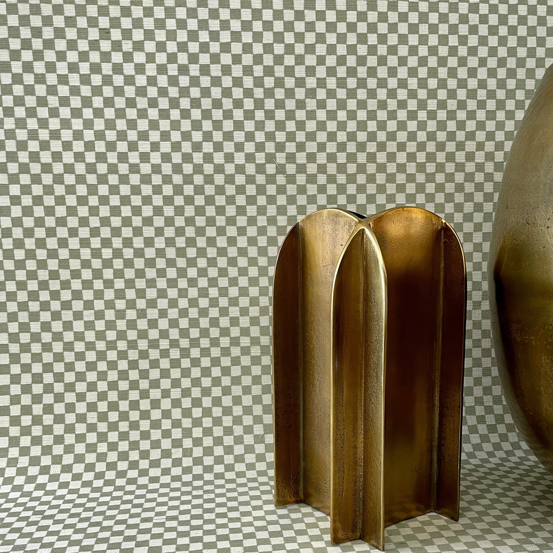 Decorative setup with grasscloth olive green checkered wallpaper covering both the wall and surface, complemented by metallic gold sculptural objects for a modern touch.
