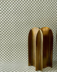 Decorative setup with grasscloth olive green checkered wallpaper covering both the wall and surface, complemented by metallic gold sculptural objects for a modern touch.