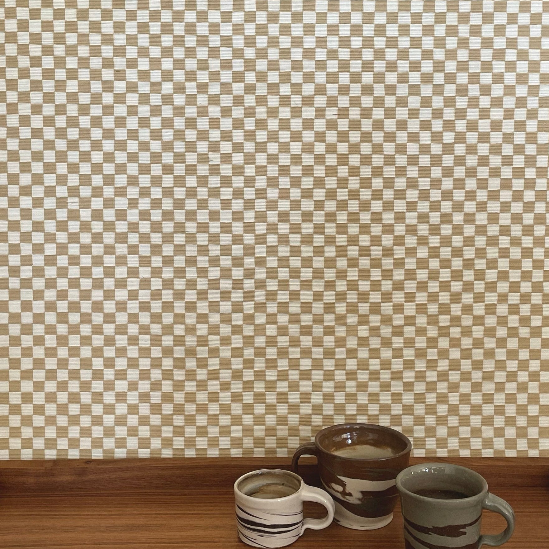 Beige and white checkered wallpaper with a woven texture, styled with handcrafted ceramic cups on a wooden surface.