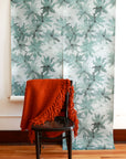 Light blue floral wallpaper displayed in hanging panels; black wooden chair with an orange woven throw draped over it in the foreground.