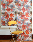 floral patterned wallpaper with red, orange and blue flowers, displayed in hanging panels; mustard-yellow folding chair placed in front for scale and contrast.