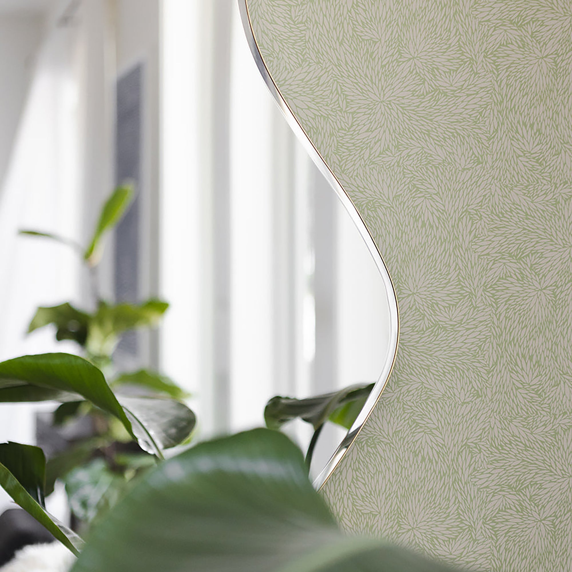 Modern interior with a soft green wallpaper featuring a delicate botanical leaf pattern, partially reflected in a curved mirror, surrounded by lush greenery.