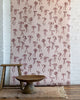 Vintage-inspired wallpaper with hand-drawn red bows on a soft pink background, styled with rustic wooden furniture and a neutral woven rug.