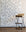 Elegant wallpaper featuring hand-drawn blue bows on a crisp white background, complemented by a beige cushioned stool with black metal legs.