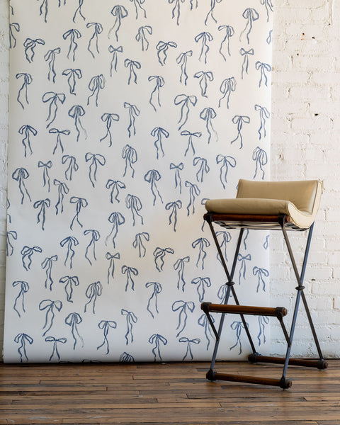 Elegant wallpaper featuring hand-drawn blue bows on a crisp white background, complemented by a beige cushioned stool with black metal legs.