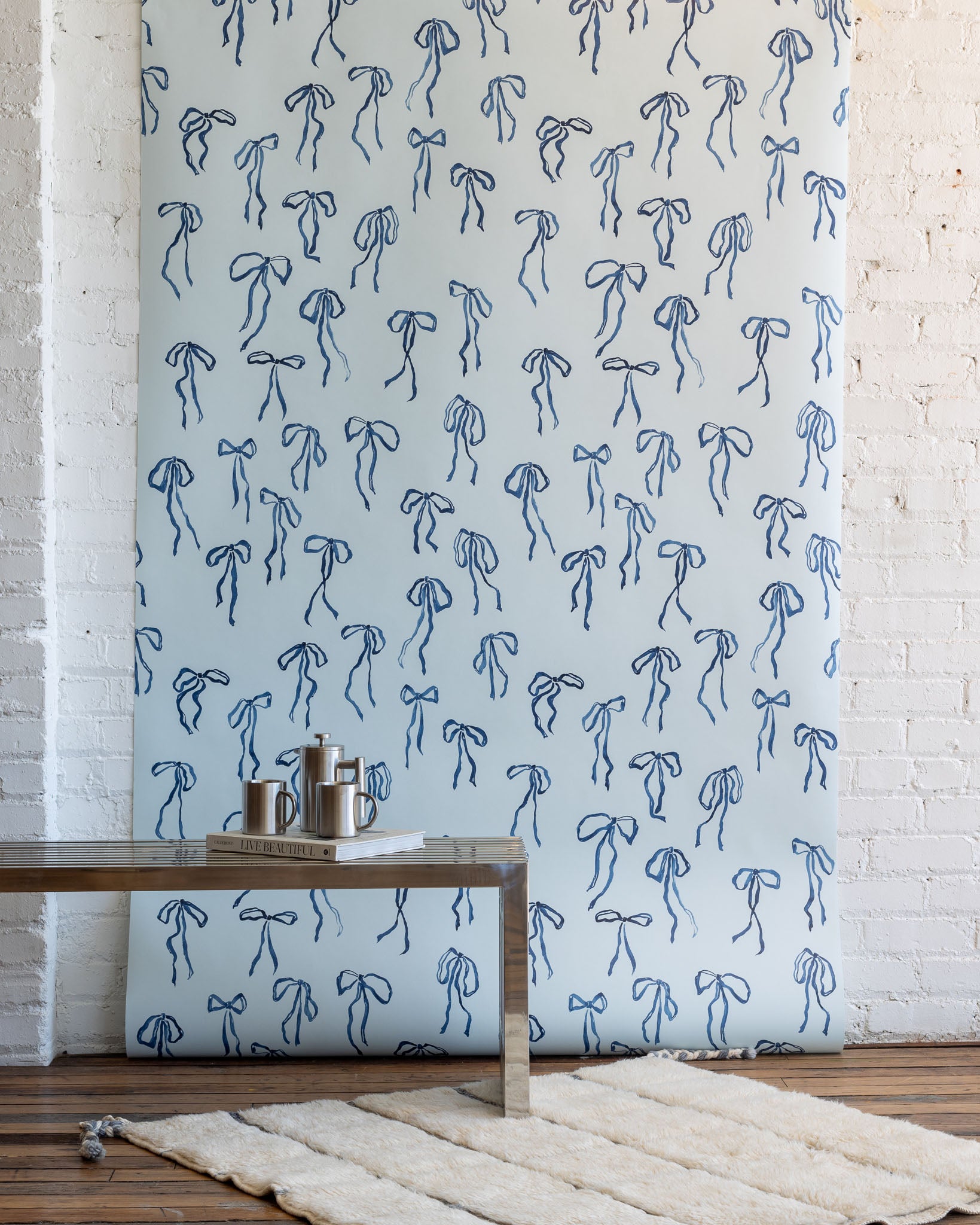Charming wallpaper with hand-drawn blue bows on a pale blue background, styled with a modern metallic coffee table and a plush white rug.