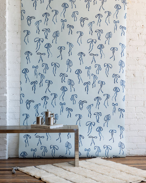 Charming wallpaper with hand-drawn blue bows on a pale blue background, styled with a modern metallic coffee table and a plush white rug.