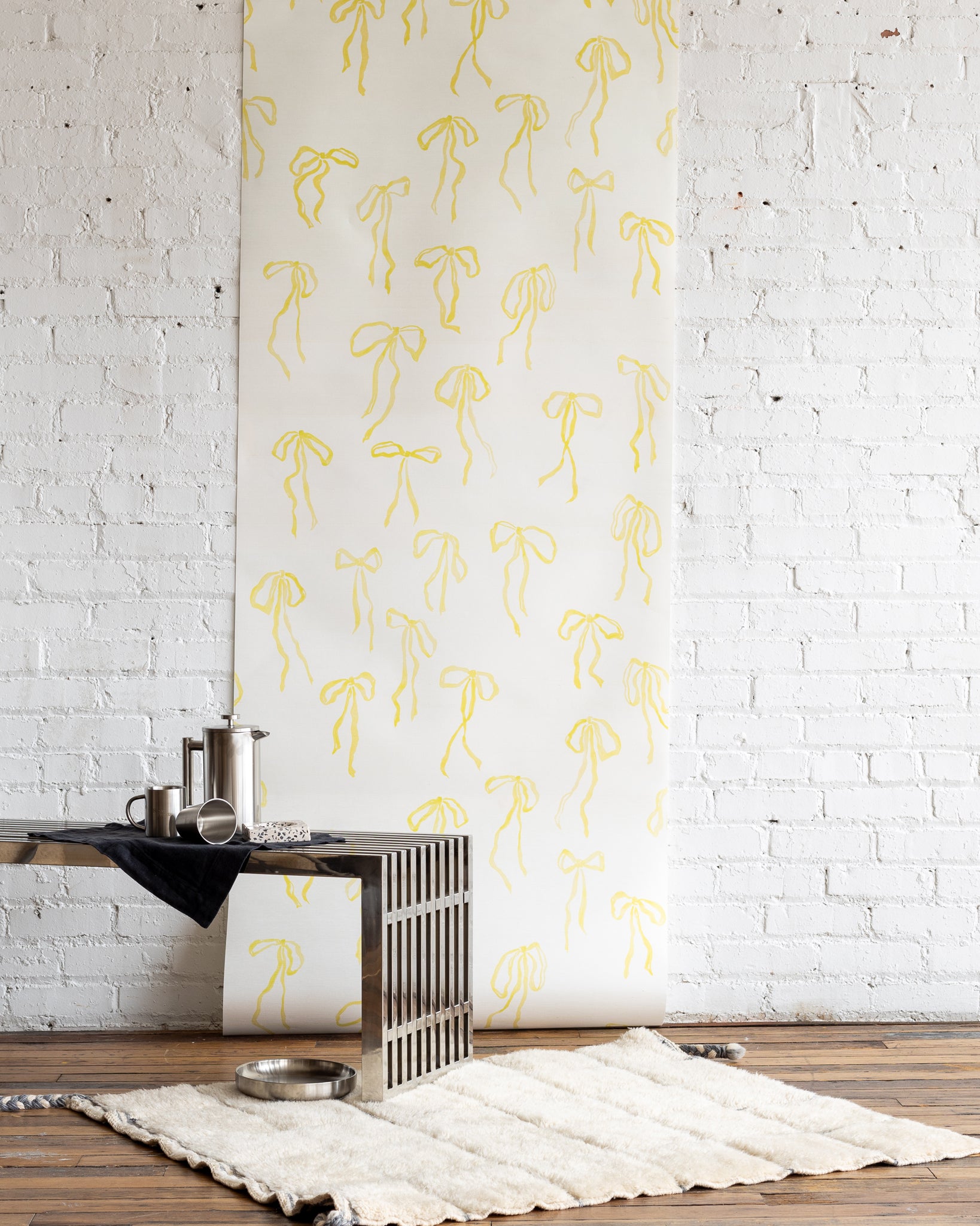 Cheerful wallpaper with hand-drawn yellow bows on a white background, styled with a modern metallic coffee table and a cozy cream rug.