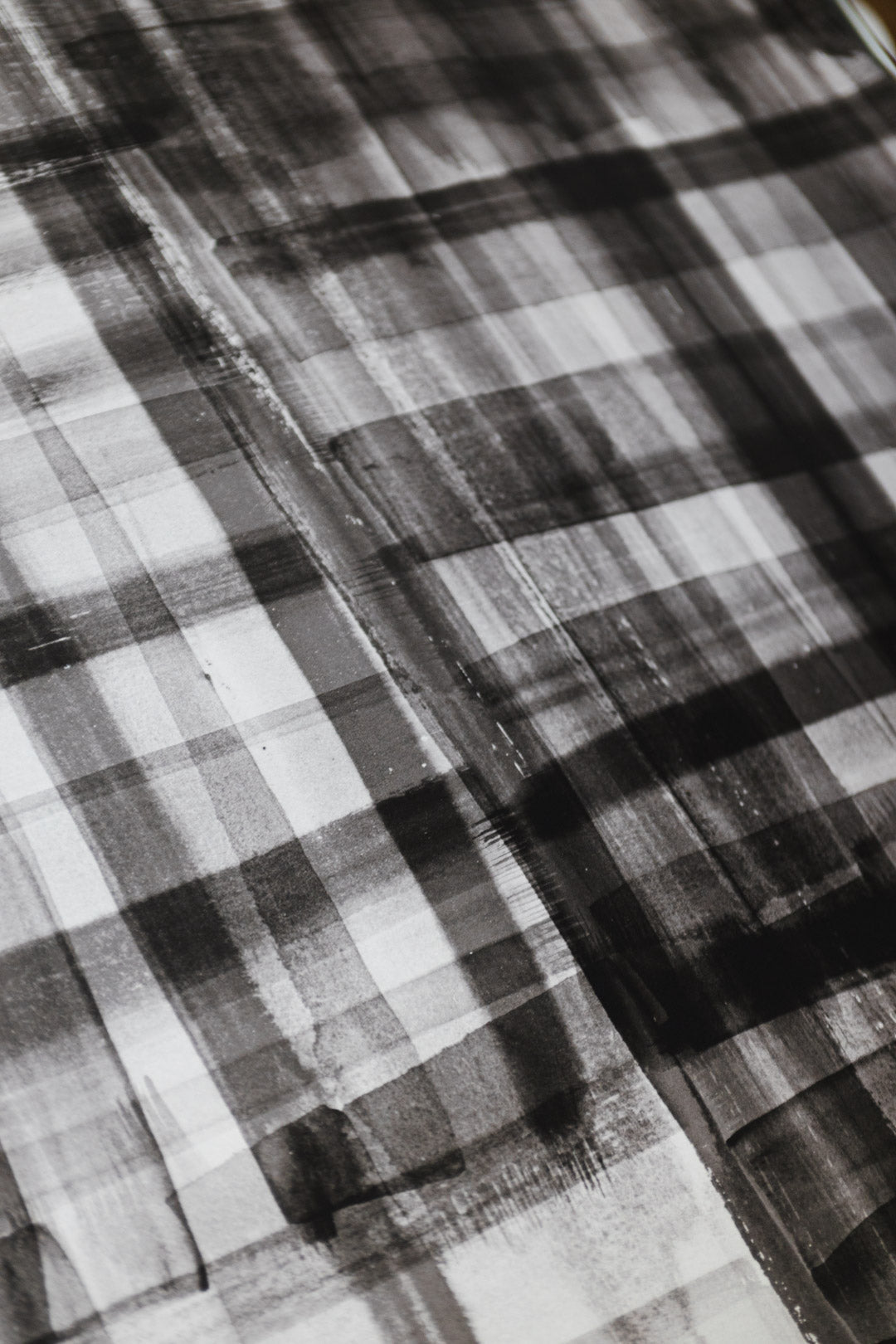 Close-up of black and white plaid wallpaper with a hand-painted, watercolor-like texture, featuring soft brushstrokes and layered transparency.