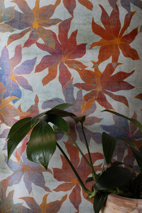 wallpaper with large abstract neutral floral pattern in warm orange, red, and blue tones; green houseplant leaves in a ceramic planter in the foreground.