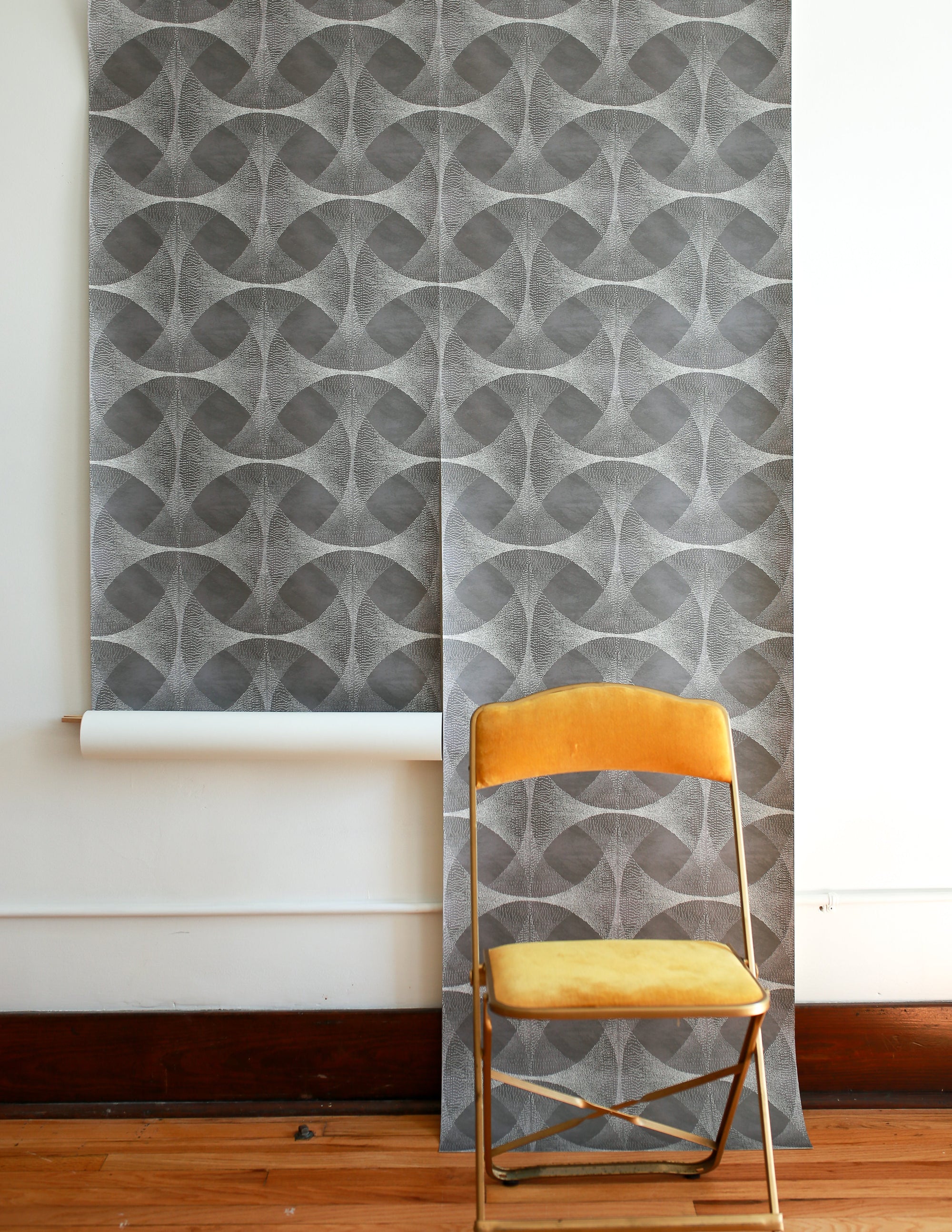 Gray geometric wallpaper with curved circular overlapping shapes, featuring delicate dotted texturing and abstract interconnected design, with yellow folding chair in foreground