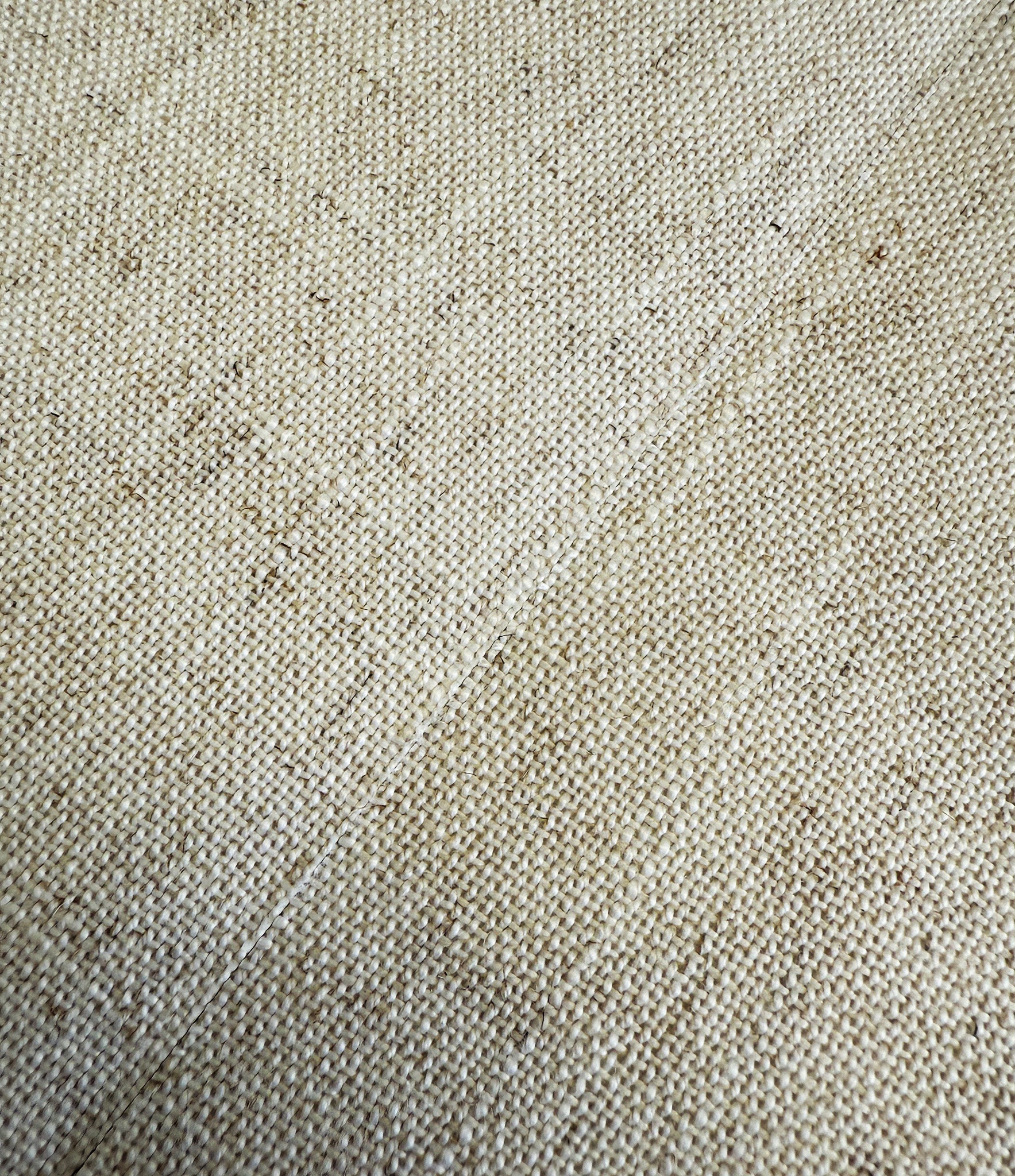Close-up of a beige woven fabric with a textured surface and seam, featuring a tight, uniform weave pattern and subtle variations in color.