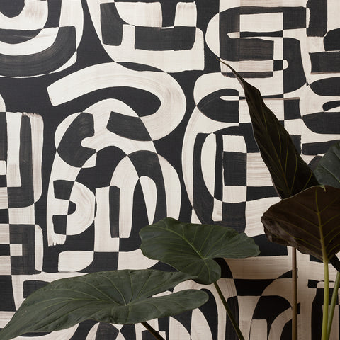 Close-up of black and white grasscloth wallpaper with bold, abstract brushstroke patterns, partially obscured by large green tropical leaves.