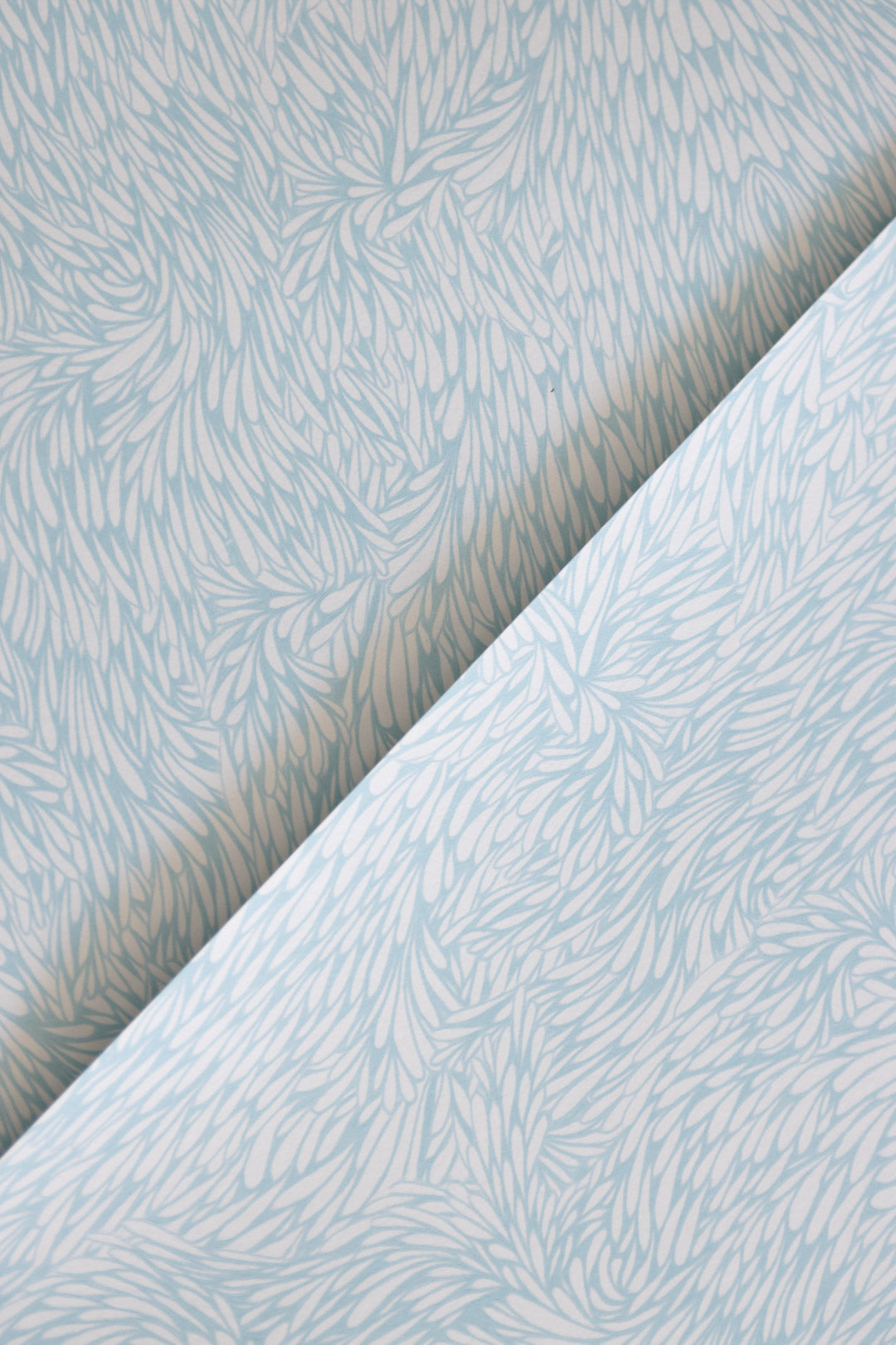 A folded section of blue wallpaper with a delicate, nature-inspired feather motif, highlighting the intricate design.